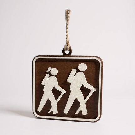 Walnut wood hiking trail sign ornament with female and male hiker silhouettes photographed on a clean white background.