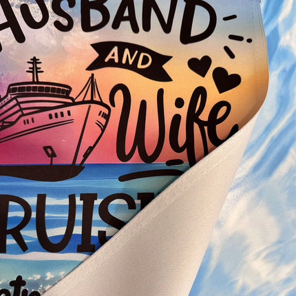 Close-up image of a cruise door banner made from premium triple-ply polyester material. The design shows part of the text “Husband and Wife Cruising” with a cruise ship graphic and hearts on a sunset ocean background. The corner is folded to display the durable fabric texture and stitching.