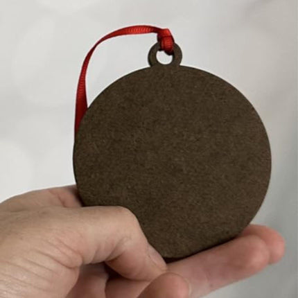 Back view of a wooden ornament held in hand, showing the smooth unfinished surface. A red ribbon is attached at the top for hanging. This image highlights the plain back of the ornament, which can be left as-is or customized by the buyer if desired.