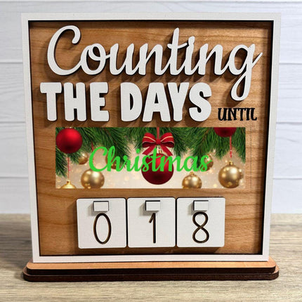 Wooden interchangeable countdown sign displaying “Counting The Days Until” with Christmas plate featuring ornaments and greenery, and number tiles showing 018 on a tabletop stand.